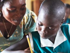 A student writes with a pencil while a teacher is nearby