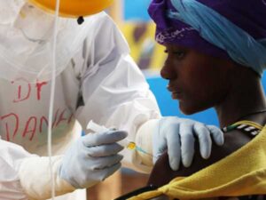 A woman receives a vaccination in her shoulder by a person in protective gear