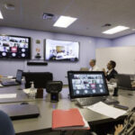 A group of people in a conference room participate in a virtual meeting