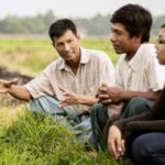 Three people sit in a field talking