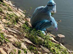 A person in protective gear takes a water sample