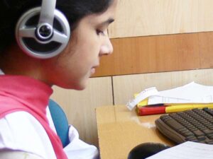 A woman wearing headphones sits at a desktop computer