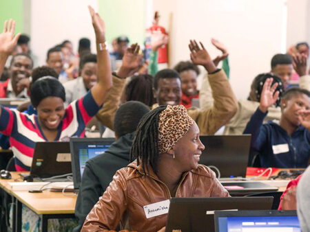 Adults smile and throw their hands in the air while sitting in front of desktop computers