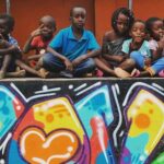 Kids sit together in front of a colorful mural.