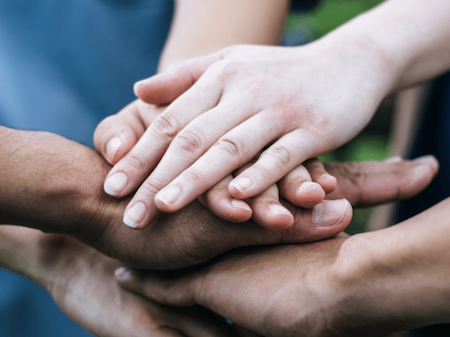 People pile their hands on each other's in a gesture of teamwork.